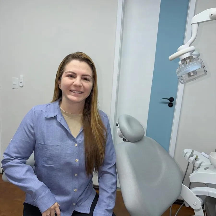 Dra. Daiane Cristo ao lado da cadeira odontológica